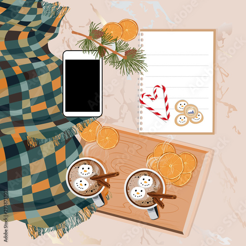 Flat lay cup of chocolate with cinnamon, marshmallow snowman and dries orange slices on wooden tray, Mobile phone, notebook, candy cane and pine branch with cones, Hot  drink for autumn or Winter