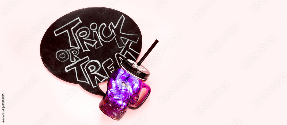 Obraz premium Halloween flat lay, woman's hand holds a glass with a skull-shaped drink and the inscription trick or treat on a pink background
