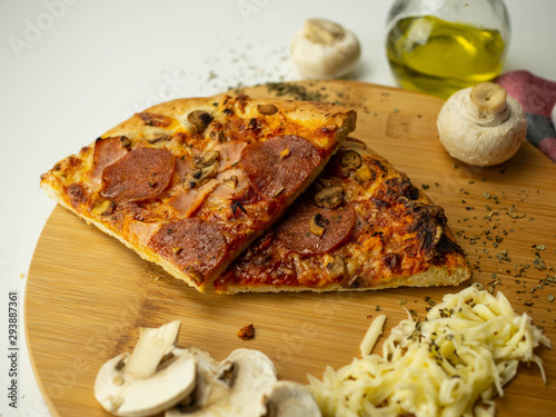 Mrożona pizza przygotowana w domu. Ser, oliwa, pieczarki, salami. Widok z góry, białe tło.