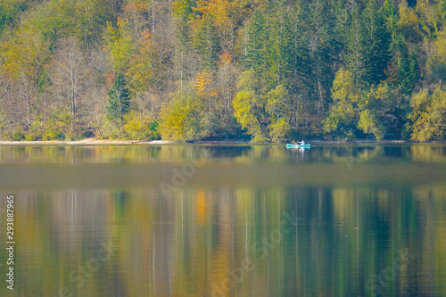 Tourists far in the distance paddle a canoe across the tranquil lake Bohinj.