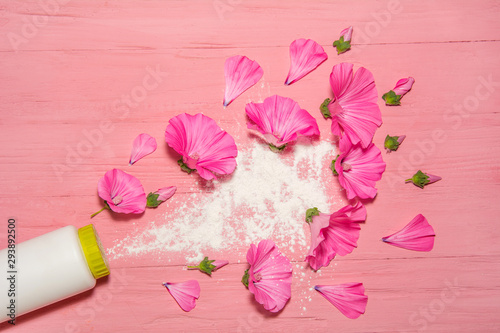 perfumed talcum powder for legs. white bottle with a salt cap top view. scattered talcum powder on a pink wooden board with pink flowers around the perimeter. white powder fragrance for the feet