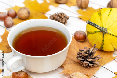Cup of tea with autumn leaves and season fruit and vegetables on white wooden table. Autumn background. Close up.