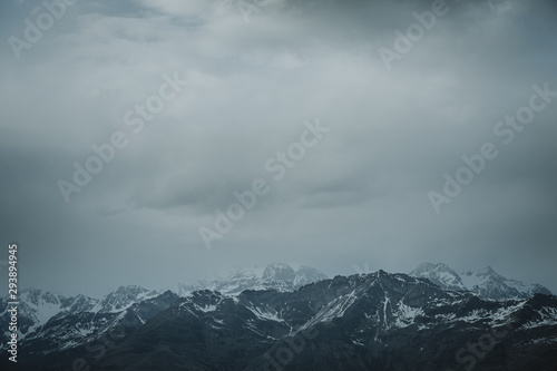 Storm is coming with dark grey clouds over the horizon of the snowy peaks of the Italian Alps in bottom part of an image and bigger part of negative space in upper part © Tomáš Hudolin
