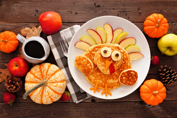 Thanksgiving breakfast table scene with turkey pancakes. Top view against a rustic wood background.