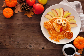 Cute Thanksgiving turkey pancakes. Top view corner border against a rustic wood background with copy space.