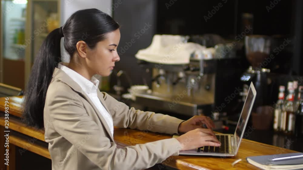 Young asian businesswoman in elegant suit typing on laptop computer at the bar counter in cafe Young asian businesswoman in elegant suit typing on laptop computer at the bar counter in cafe