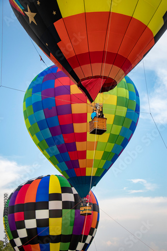 Brightly colored hot air balloons hover tethered above the ground while passengers enjoy the view in the warm afternoon sunlight.