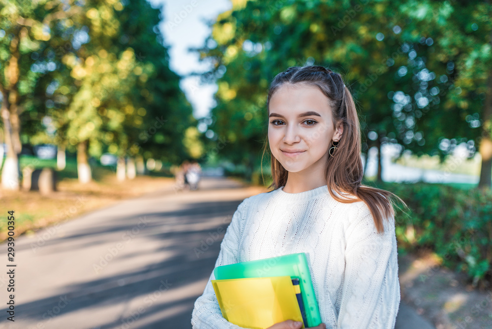 beautiful teenager girl 13-15 years old, in a white sweater park, holds notebooks folders textbooks hand. Free space text learning school college. Education children study city. Happy schoolgirl. beautiful teenager girl 13-15 years old, in a white sweater park, holds notebooks folders textbooks hand. Free space text learning school college. Education children study city. Happy schoolgirl.