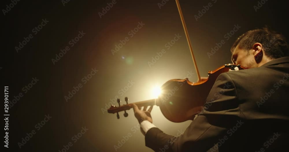 Male violin player having a solo on stage. Professional musician wearing tux is spotted by light on black background 4k footage