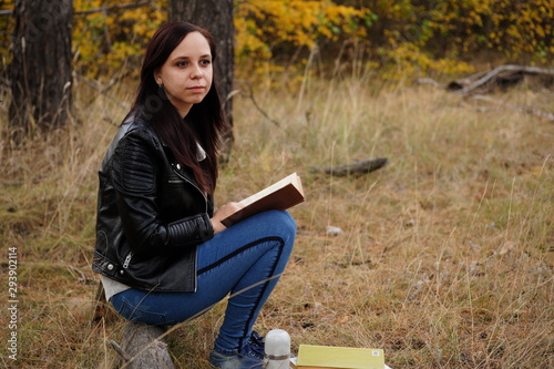 Beautiful woman reading a book in the autumn forest. A woman sits near a tree in an autumn forest and holds a book. Girl reading a book. Autumn season concept and reading