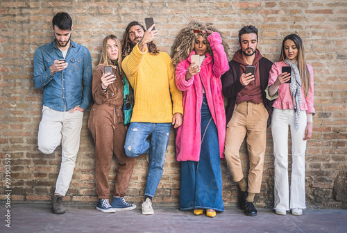 Group of young multiracial people smartphone and social media addicted standing on a brick wall. Millennials people using smartphones and new technologies