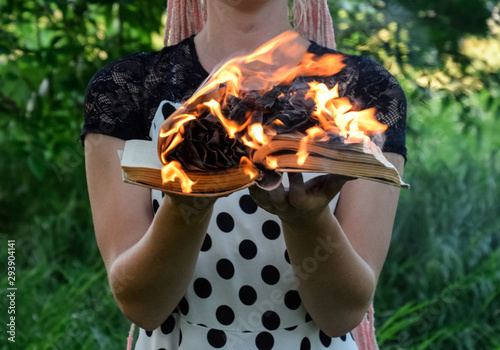 girl holds a burning book in her hands. A young woman in a forest burns a book. photo