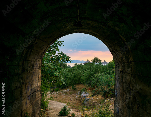 Blick durch einen Tunnel auf einen Sonnenuntergang an der Adriak  ste mit Sonnenliege und Sonnenschirm 