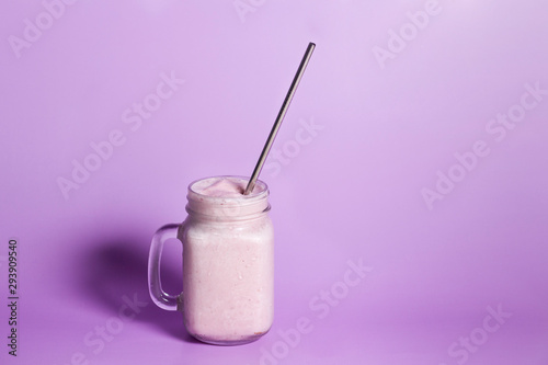 Strawberry smoothie drink in mason jar glass with reusable stainless steel straw on purple background
