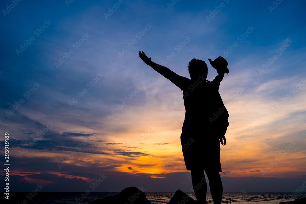 Traveler backpacker of freedom style Concept: Silhouette of Asian Young woman relaxing standing on rock seabeach, Strong confidence open her arms and watching sunset scene in summer sunset sky outdoor