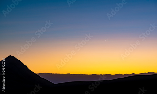 USA, Nevada, Nye County, Death Valley National Park. A High contrast blue orage yellow sunset background with fingernail moon that looks like another planet from a sci fi flick.