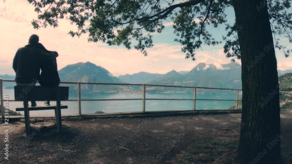 Silhouette of a romantic couple sitting in a bench in a panoramic point of view of the Lecco Lake, Italy. 4k