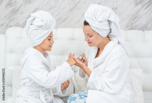 Young woman and her daughter are doing manicures at home. Mom and child girl are in bathrobes and with towels on their heads