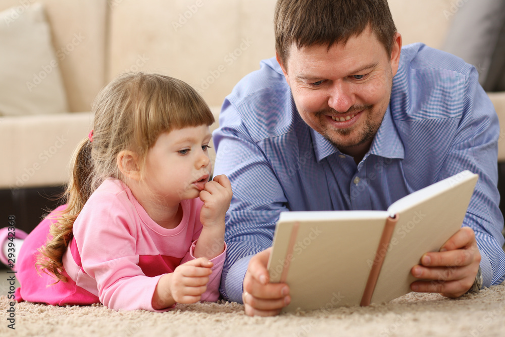 Daughter father reading book lying on carpet in living room in front of the sofa concept