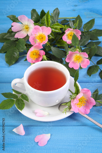 Cup of hot tea and wild rose flower on blue boards