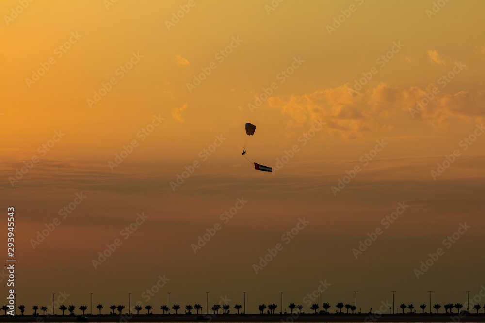 a man flying at the sunset holding uae flag, uae flag waving at the sunset, Flying paraglider with uae flag , uae flag day. united arab emirates 