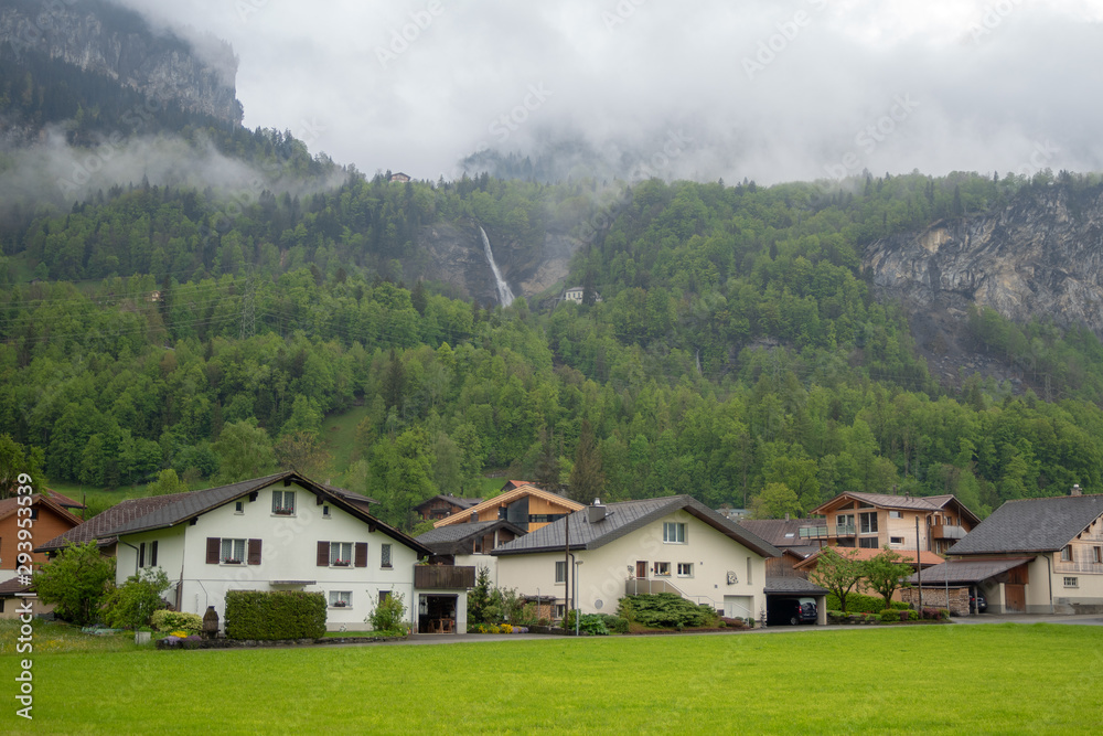 Houses beside the misty mountain full of fresh green trees with waterfall in rural area of Switzerland for background and copy space