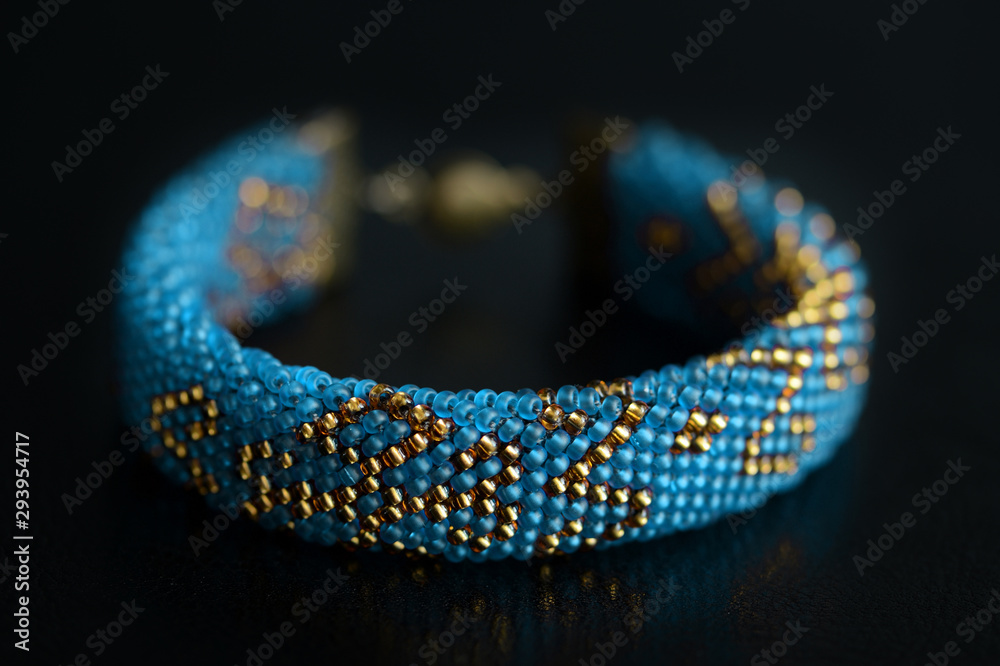 Fototapeta premium Beaded bracelet blue color with golden pattern on a dark background close up