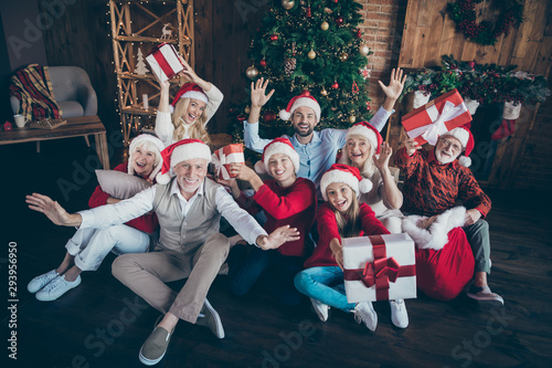 Portrait of nice lovely cheerful big full family brother sister couples wearing cap hat headwear sitting on floor holding in hands gifts waving hi hello tradition loft industrial style interior house