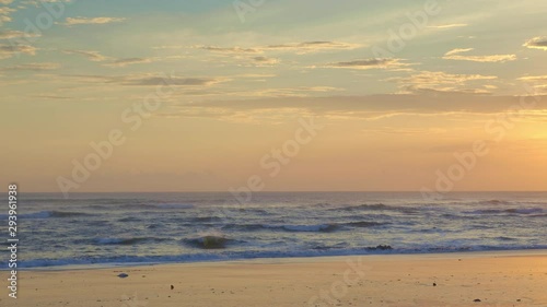 Beautiful wet sandy beach during yellow sunset with big waves and foggy background