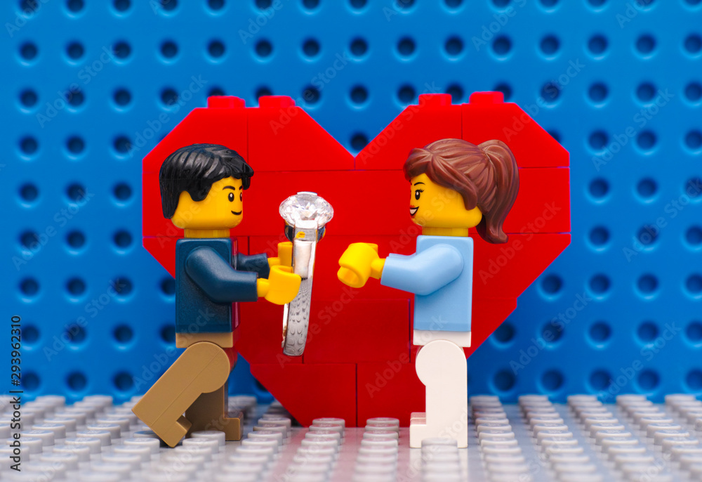 Foto Stock Tambov, Russian Federation - September 03, 2015 Lego man with  ring makes marriage proposal to his girl standing in front of heart on Lego  gray baseplate. Studio shot.