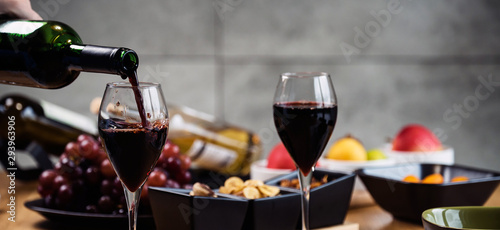 Red wine pouring into a wine glass at a tasting with various types of appetizers. 