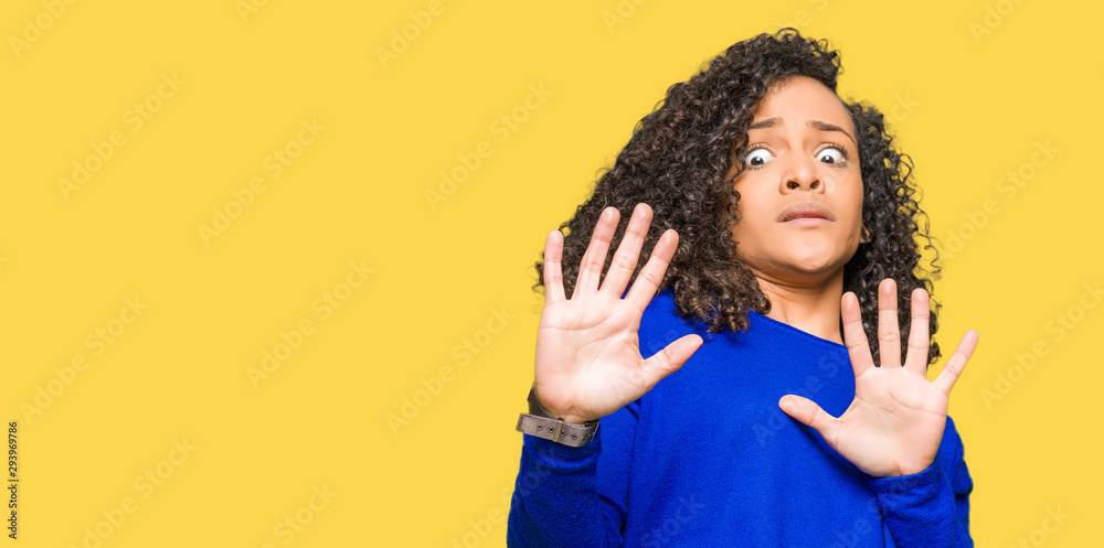 Young beautiful woman with curly hair wearing winter sweater afraid and terrified with fear expression stop gesture with hands, shouting in shock. Panic concept. Young beautiful woman with curly hair wearing winter sweater afraid and terrified with fear expression stop gesture with hands, shouting in shock. Panic concept.