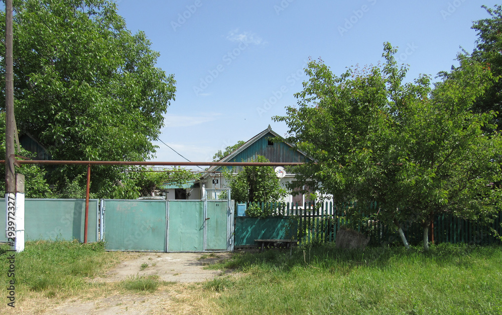 Wooden country house behind a blue fence among the green trees.