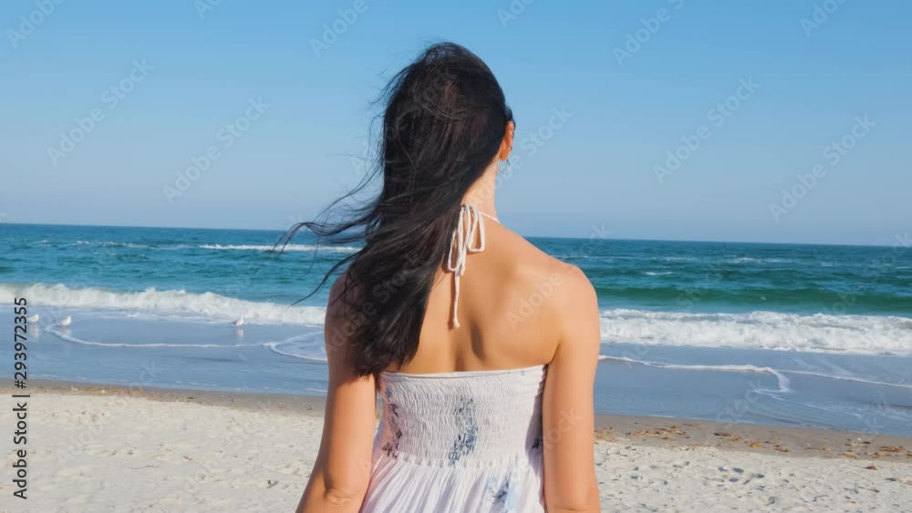 Young beautiful woman dressed in a white dress walk barefoot on the summer beach Young beautiful woman dressed in a white dress walk barefoot on the summer beach