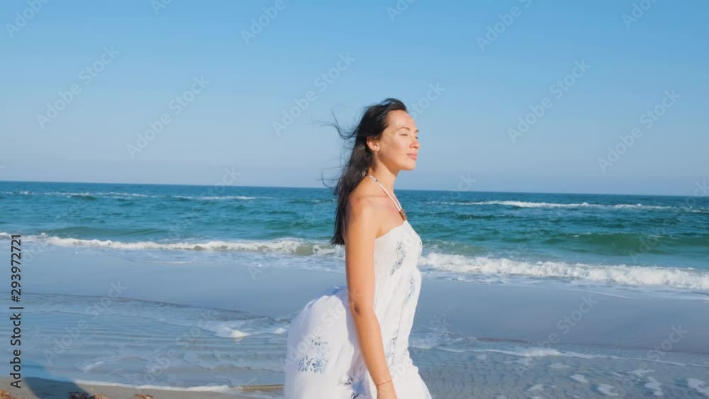 Young beautiful woman dressed in a white dress walk barefoot on the summer beach Young beautiful woman dressed in a white dress walk barefoot on the summer beach
