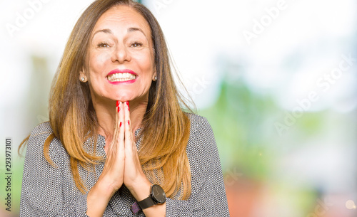 Beautiful middle age business woman praying with hands together asking for forgiveness smiling confident.