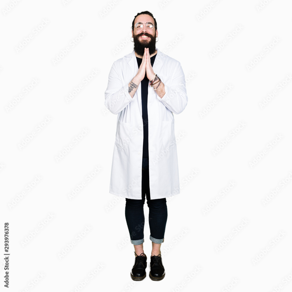 Doctor therapist man with long hair and bear wearing white coat praying with hands together asking for forgiveness smiling confident.
