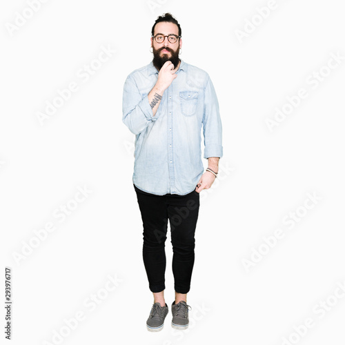 Young hipster man with long hair and beard wearing glasses looking confident at the camera with smile with crossed arms and hand raised on chin. Thinking positive.