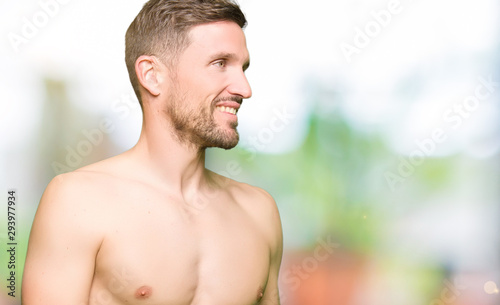 Handsome shirtless man showing nude chest looking away to side with smile on face, natural expression. Laughing confident.