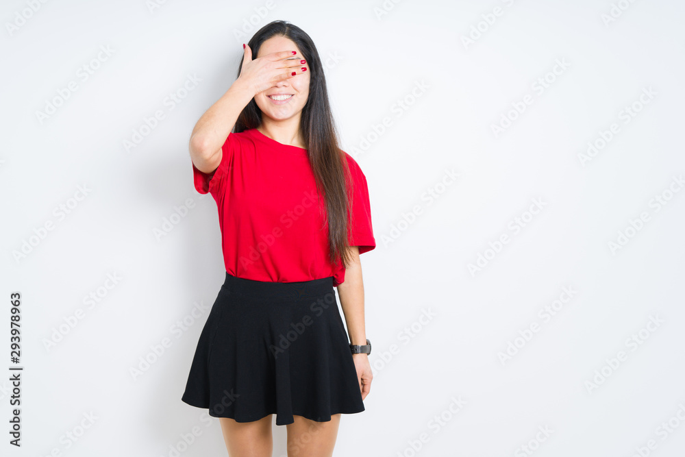 Beautiful brunette woman wearing red t-shirt and skirt over isolated background smiling and laughing with hand on face covering eyes for surprise. Blind concept. Beautiful brunette woman wearing red t-shirt and skirt over isolated background smiling and laughing with hand on face covering eyes for surprise. Blind concept.