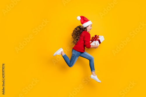 Full length profile photo of amazed small lady jumping high taking giftbox from santa in x-mas midnight wear red knitted sweater and jeans isolated yellow background
