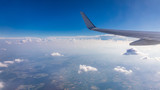 View of the wing of an airplane flying above the clouds at high altitude under a blue sky from the passenger window. In flight over Europe. View of jet airplane wing flying in blue sky over clouds.