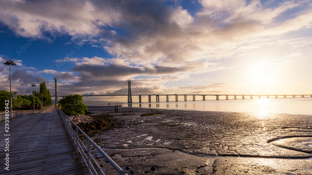 Vasco da Gama bridge at sunrise in Lisbon, Portugal. Vasco da Gama Bridge is a cable-stayed bridge flanked by viaducts and rangeviews that spans the Tagus River in Parque das Nações in Lisbon.