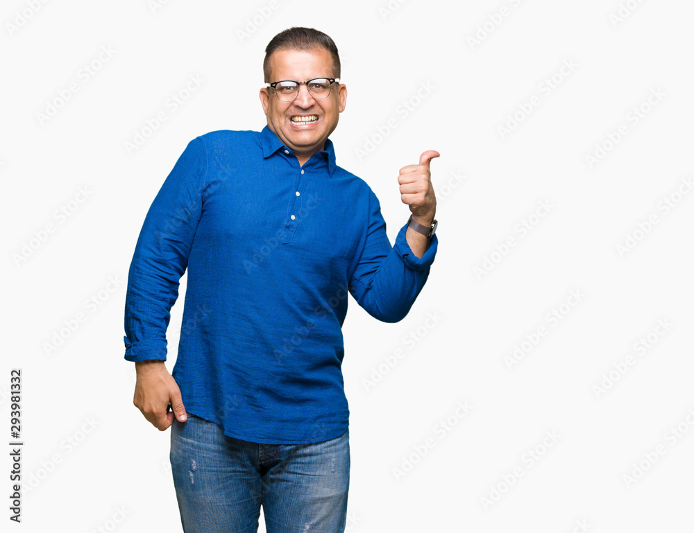 Middle age arab man wearing glasses over isolated background smiling with happy face looking and pointing to the side with thumb up. Middle age arab man wearing glasses over isolated background smiling with happy face looking and pointing to the side with thumb up.