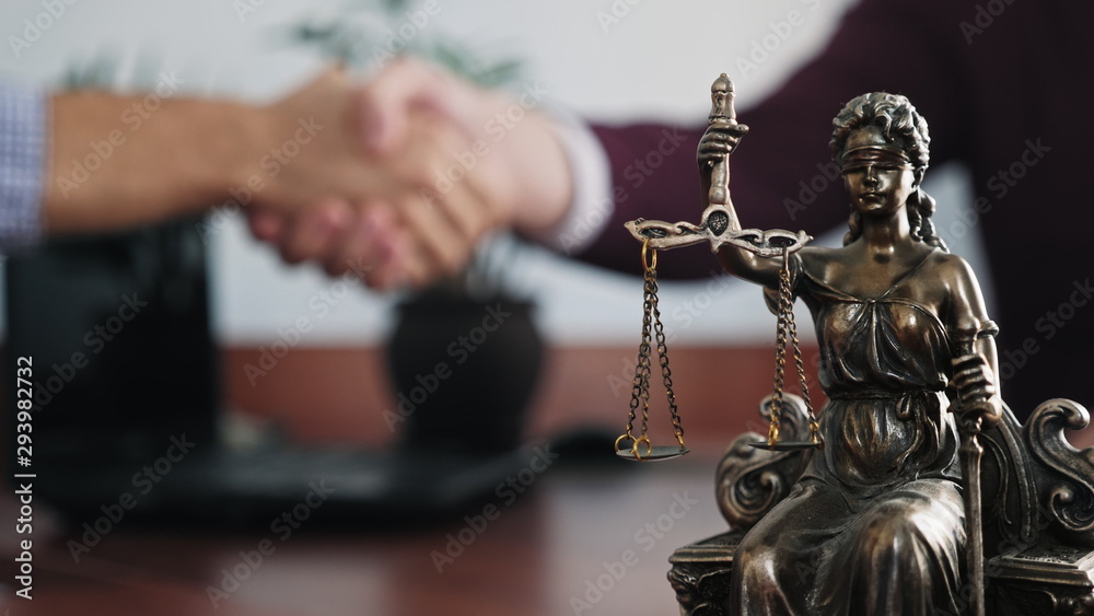 Statuette of lady justice on the table close-up on a blurred background of two men handshaking