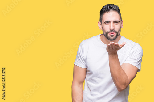 Young man wearing casual white t-shirt over isolated background looking at the camera blowing a kiss with hand on air being lovely and sexy. Love expression.