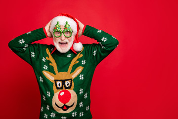 Photo of funny grey haired santa overjoyed with children and relatives coming to newyear party wear specs x-mas tree shape ugly ornament reindeer sweater isolated red background