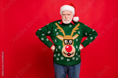 Bad angry santa claus for naughty kids concept. Portrait of sullen grumpy old man in x-mas headwear have conflict on christmas time wear fun reindeer decor sweater isolated red color background