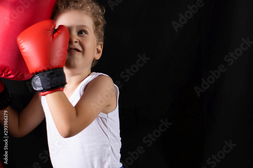 A little boy in red boxing gloves trains to hit the boxing bag. Sports, children's boxing. © Elena