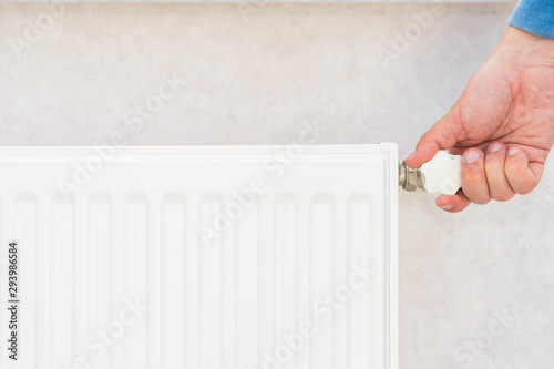 Male hand regulates the thermostat knob on the white heating radiator with at home a cold season.